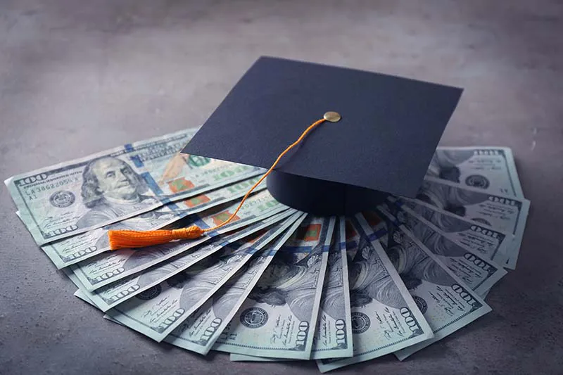 graduation hat on top of hundred dollar bills
